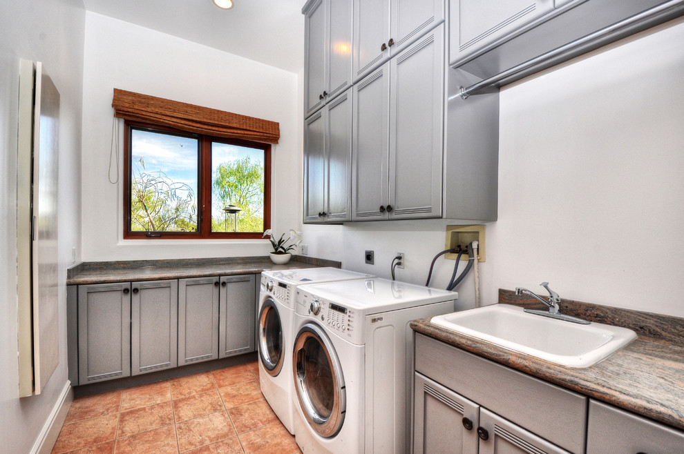 Große Klassische Waschküche in L-Form mit flächenbündigen Schrankfronten, grauen Schränken, Granit-Arbeitsplatte, beiger Wandfarbe, Keramikboden und Waschmaschine und Trockner nebeneinander in Orange County