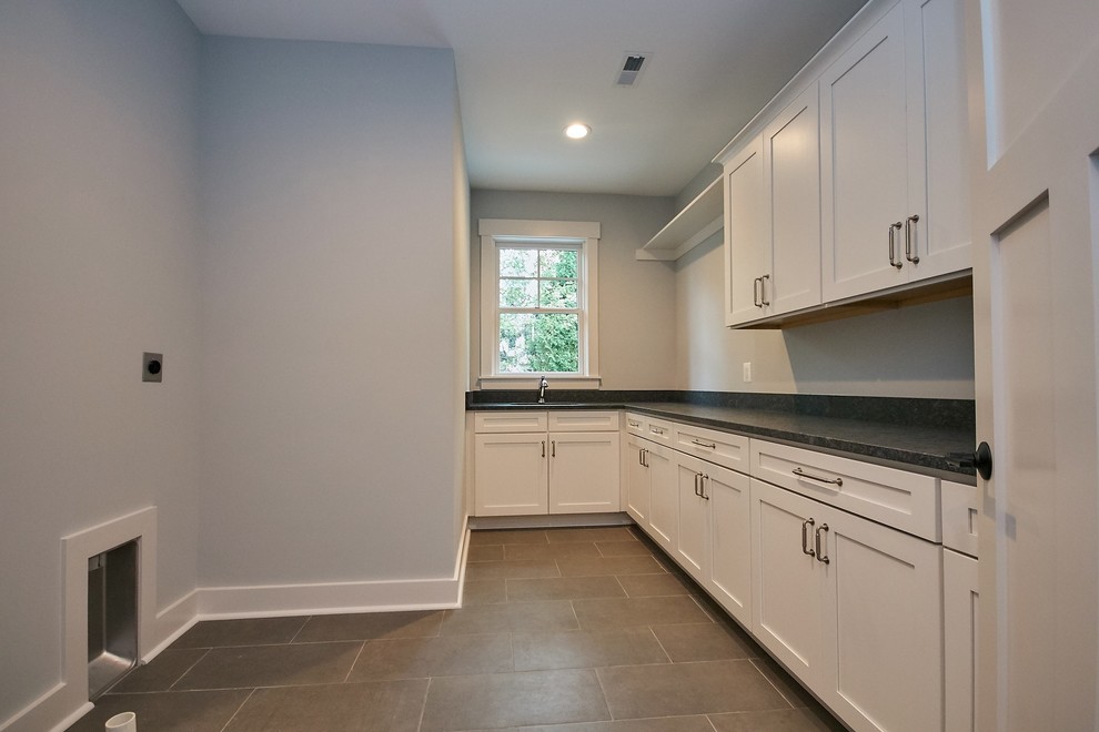 Photo of a large country l-shaped separated utility room in DC Metro with a submerged sink, shaker cabinets, white cabinets, granite worktops, grey walls, ceramic flooring, a side by side washer and dryer, grey floors and black worktops.