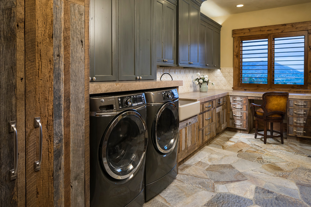 Immagine di un'ampia sala lavanderia rustica con lavello stile country, ante in legno scuro, lavatrice e asciugatrice affiancate, pavimento grigio, top marrone, ante in stile shaker e pareti beige