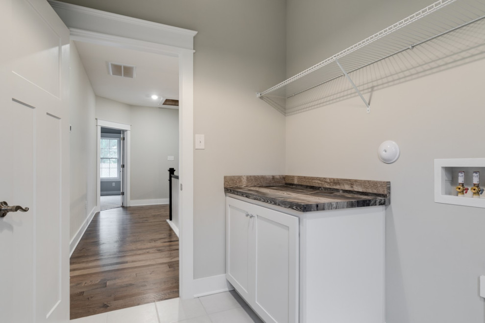 Example of a large arts and crafts single-wall ceramic tile and gray floor dedicated laundry room design in Richmond with recessed-panel cabinets, white cabinets, laminate countertops, gray walls and brown countertops