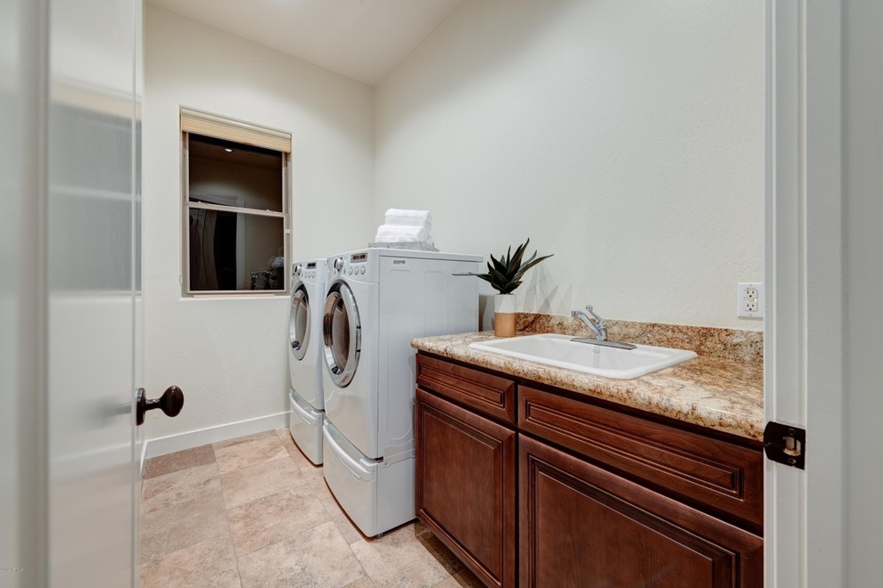 Mid-sized trendy galley travertine floor and beige floor dedicated laundry room photo in Phoenix with an utility sink, raised-panel cabinets, medium tone wood cabinets, granite countertops, beige walls, a side-by-side washer/dryer and beige countertops