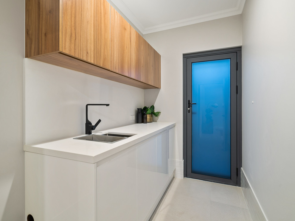Dedicated laundry room - small modern single-wall ceramic tile and beige floor dedicated laundry room idea in Perth with an undermount sink, flat-panel cabinets, medium tone wood cabinets, solid surface countertops, gray walls, a stacked washer/dryer and white countertops
