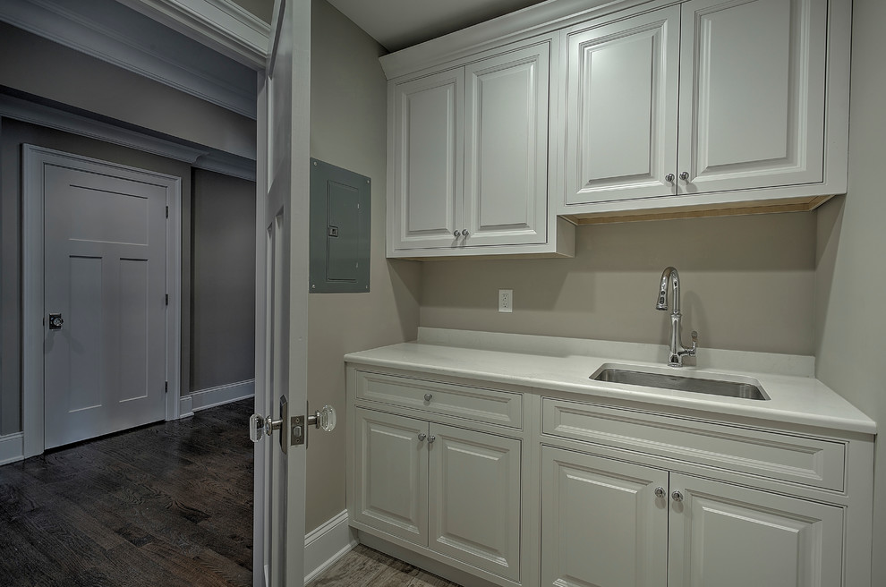 Design ideas for an expansive classic single-wall separated utility room in New York with an utility sink, raised-panel cabinets, white cabinets, engineered stone countertops, beige walls, dark hardwood flooring and a side by side washer and dryer.