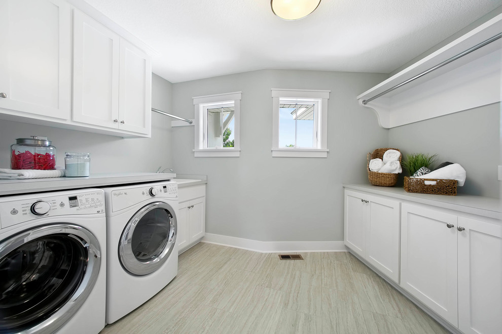 Inredning av en mellanstor grå grått tvättstuga enbart för tvätt, med en allbänk, vita skåp, grå väggar, ljust trägolv och en tvättmaskin och torktumlare bredvid varandra