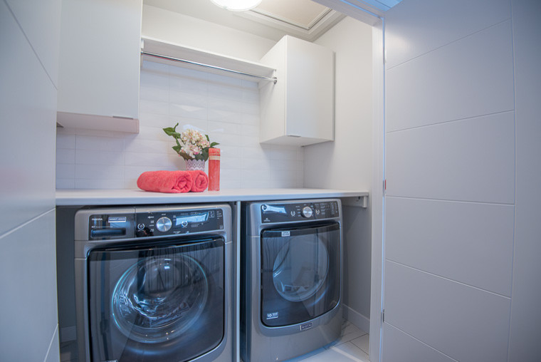 Imagen de lavadero lineal contemporáneo pequeño con armarios con paneles lisos, puertas de armario blancas, encimera de acrílico, paredes blancas, lavadora y secadora juntas y suelo blanco