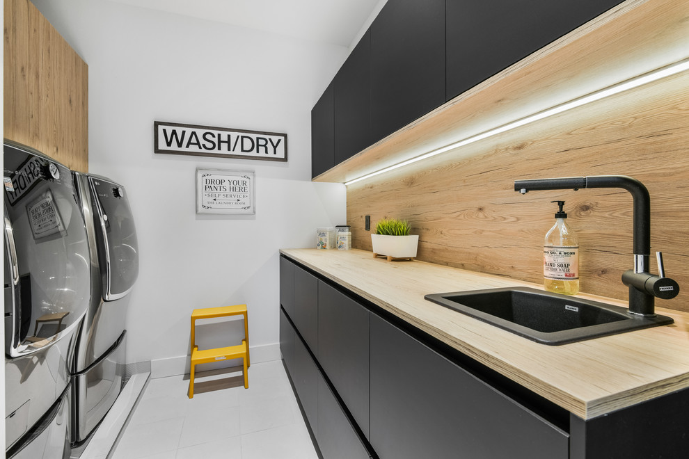 Ispirazione per una sala lavanderia contemporanea con lavello da incasso, ante lisce, ante nere, top in legno, pareti bianche, lavatrice e asciugatrice affiancate, pavimento bianco e top beige