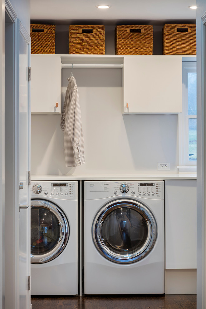 Imagen de lavadero multiusos y lineal contemporáneo pequeño con puertas de armario blancas, suelo de madera oscura, armarios con paneles lisos, encimera de acrílico, paredes blancas y lavadora y secadora juntas