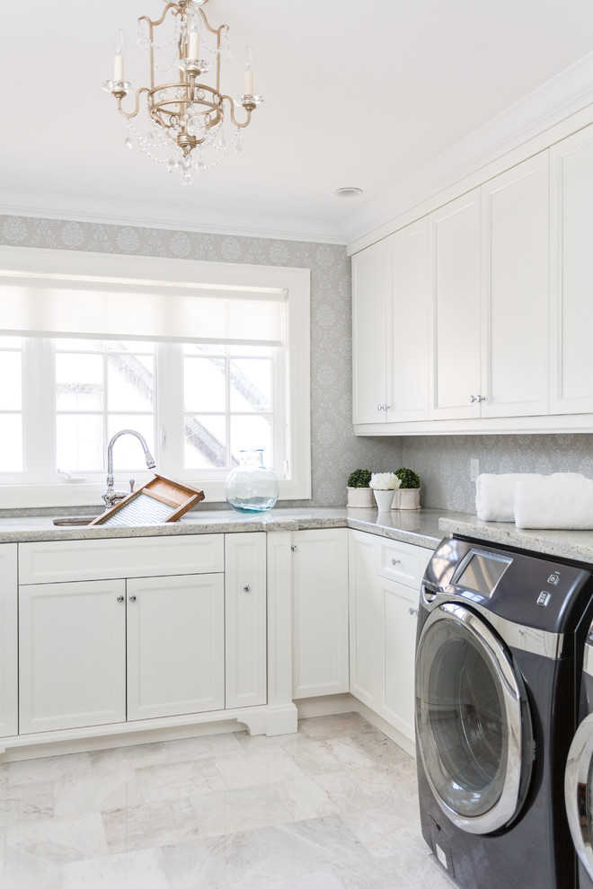 Exempel på en stor klassisk l-formad tvättstuga enbart för tvätt, med en tvättmaskin och torktumlare bredvid varandra, luckor med infälld panel, vita skåp, en undermonterad diskho, granitbänkskiva, marmorgolv och grå väggar