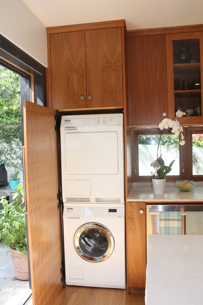 Foto de armario lavadero lineal pequeño con armarios con paneles lisos, puertas de armario de madera clara, encimera de cuarzo compacto, suelo de madera clara y lavadora y secadora apiladas