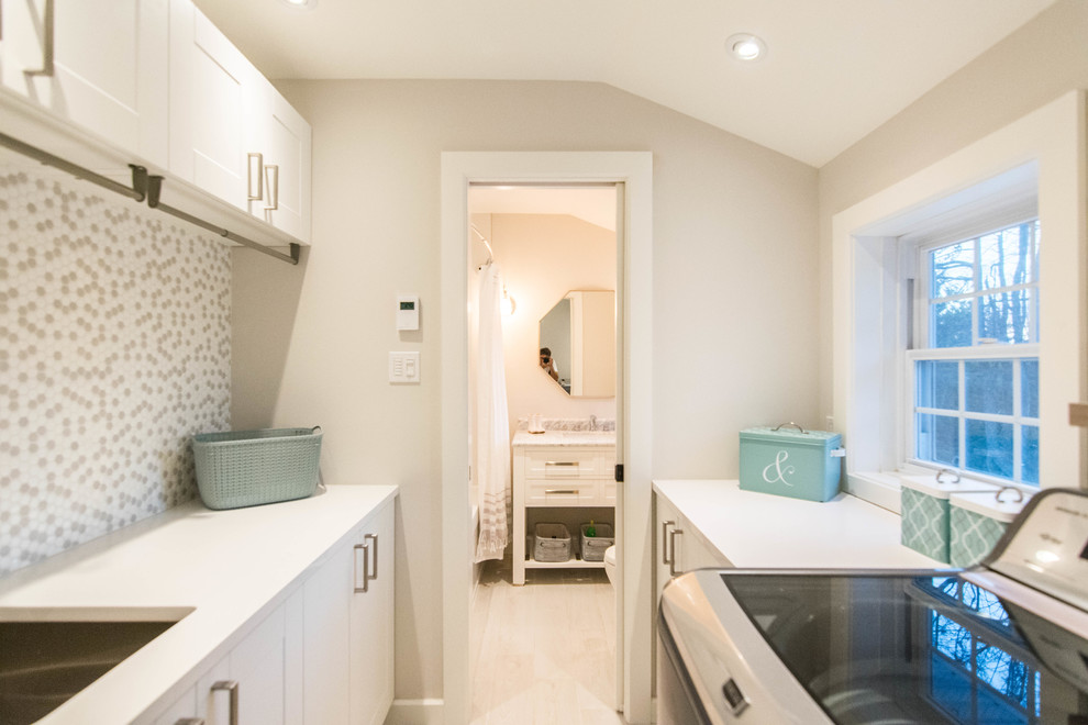Example of a large beach style galley ceramic tile and gray floor utility room design in Montreal with an utility sink, shaker cabinets, white cabinets, quartz countertops, gray walls, a side-by-side washer/dryer and white countertops