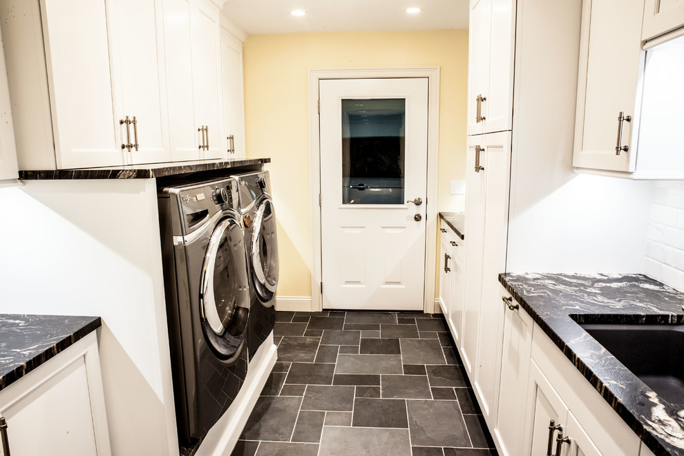 Idéer för en mellanstor klassisk parallell tvättstuga enbart för tvätt, med en undermonterad diskho, luckor med infälld panel, vita skåp, marmorbänkskiva, gula väggar, skiffergolv, en tvättmaskin och torktumlare bredvid varandra och grått golv