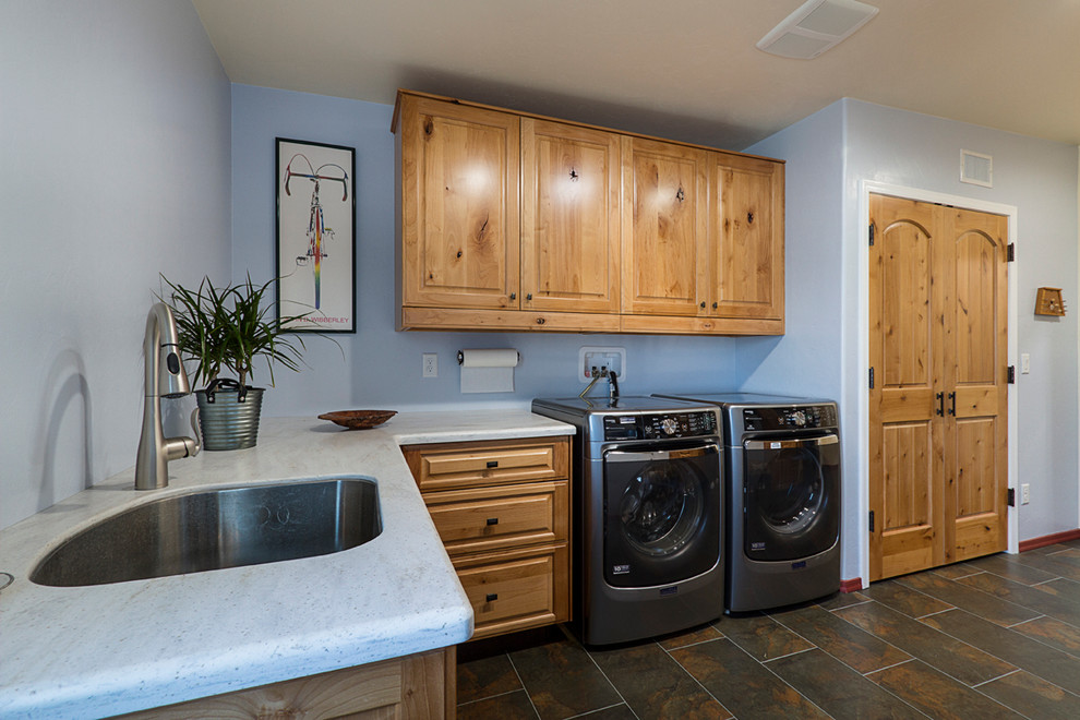 Bild på ett amerikanskt u-format grovkök, med en undermonterad diskho, luckor med upphöjd panel, skåp i mellenmörkt trä, bänkskiva i koppar, klinkergolv i porslin, en tvättmaskin och torktumlare bredvid varandra och blå väggar