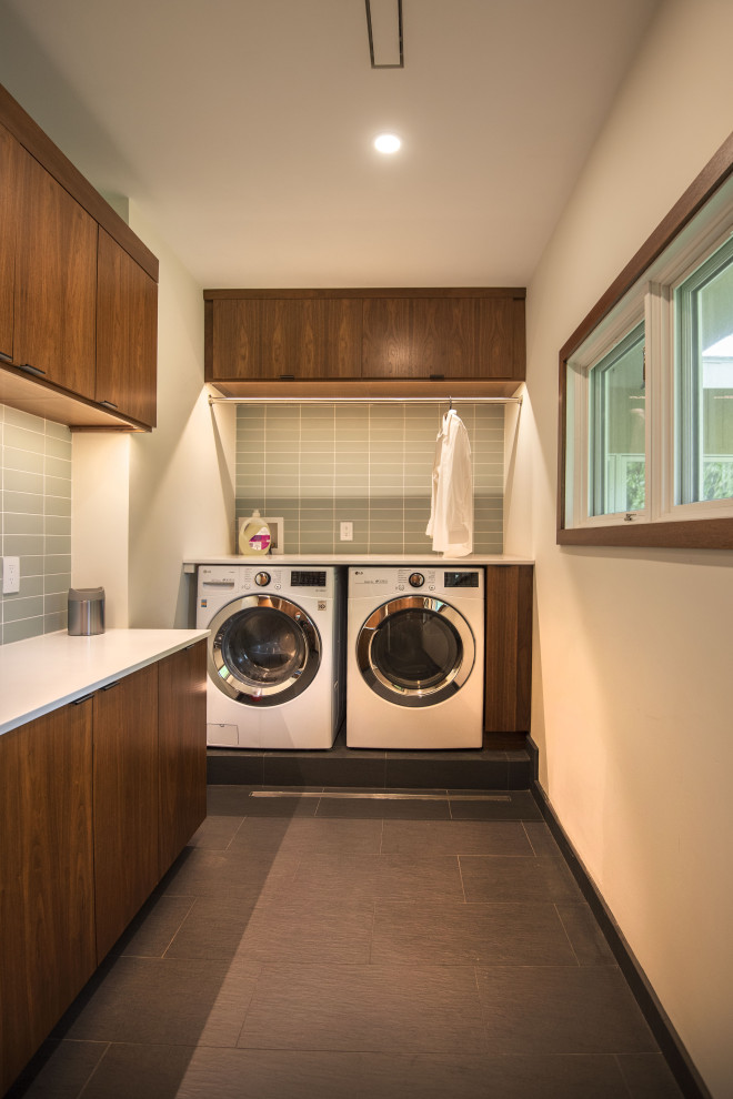 Immagine di una lavanderia moderna con ante lisce, ante in legno bruno, pareti grigie, lavatrice e asciugatrice affiancate, pavimento nero e top bianco