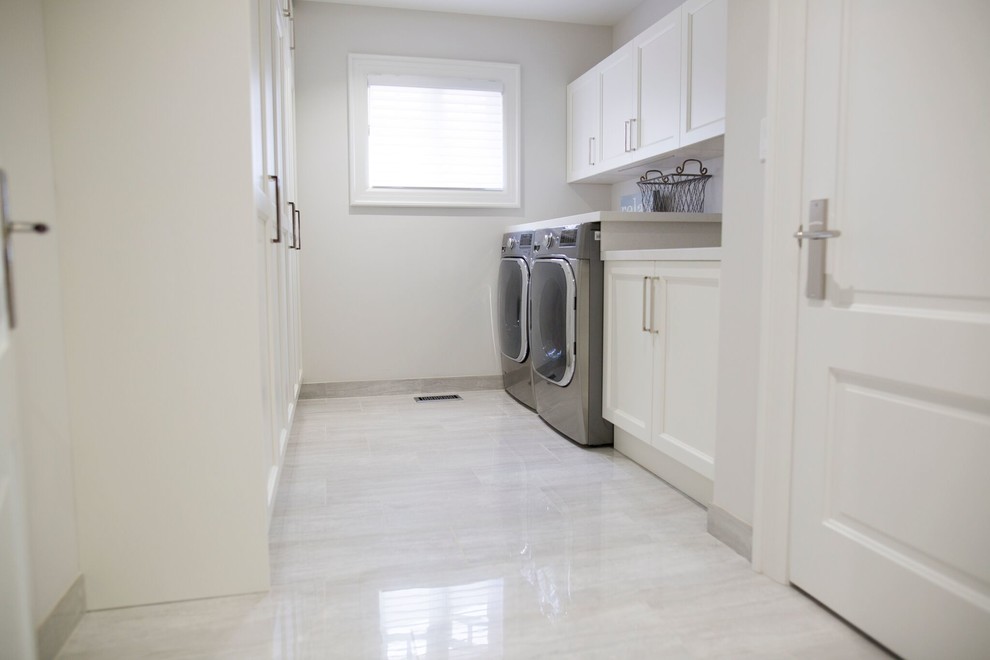 Klassisk inredning av en mellanstor linjär tvättstuga enbart för tvätt, med luckor med infälld panel, vita skåp, bänkskiva i kvarts, vita väggar, klinkergolv i porslin, en tvättmaskin och torktumlare bredvid varandra, grått golv och en undermonterad diskho