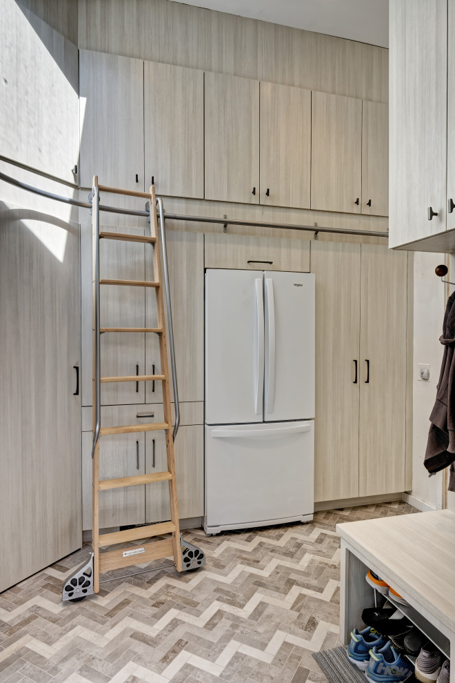 Photo of a small modern u-shaped utility room in New York with a submerged sink, flat-panel cabinets, light wood cabinets, engineered stone countertops, white walls, porcelain flooring, a side by side washer and dryer, multi-coloured floors, white worktops and a vaulted ceiling.