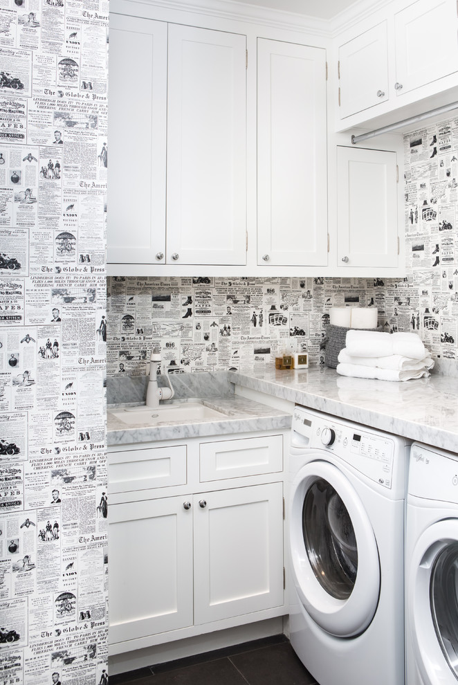Bild på en vintage grå l-formad grått tvättstuga enbart för tvätt, med en undermonterad diskho, skåp i shakerstil, vita skåp, flerfärgade väggar och en tvättmaskin och torktumlare bredvid varandra