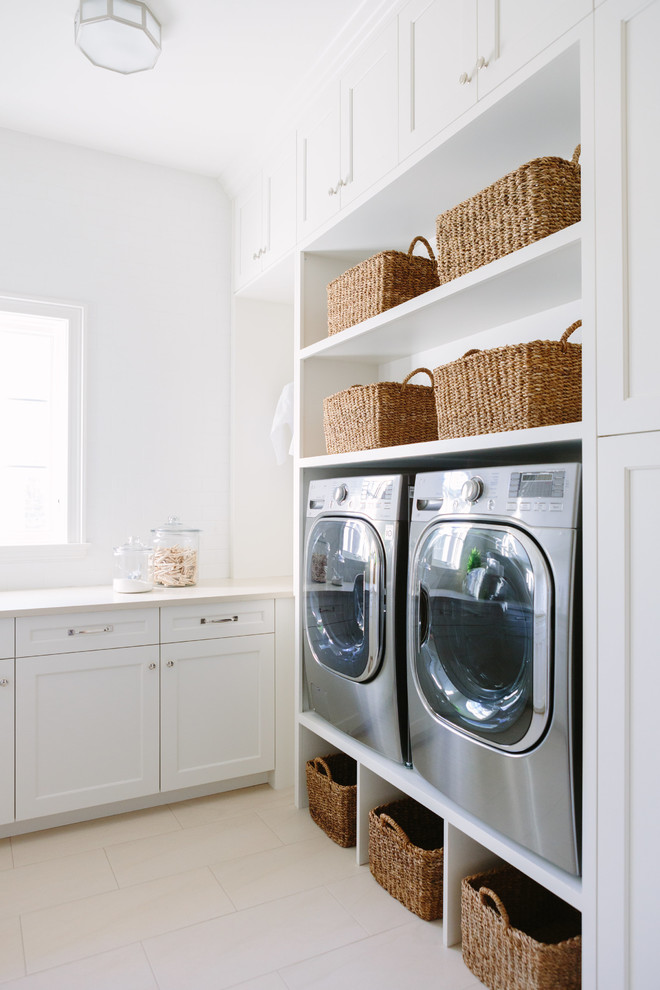 Klassisk inredning av en beige l-formad beige tvättstuga enbart för tvätt, med en undermonterad diskho, luckor med profilerade fronter, vita skåp, bänkskiva i koppar, vita väggar, klinkergolv i porslin, en tvättmaskin och torktumlare bredvid varandra och beiget golv