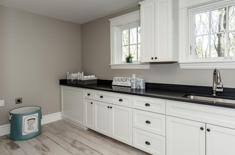 Idéer för att renovera en funkis tvättstuga, med en undermonterad diskho, luckor med infälld panel, vita skåp, granitbänkskiva, grå väggar och ljust trägolv