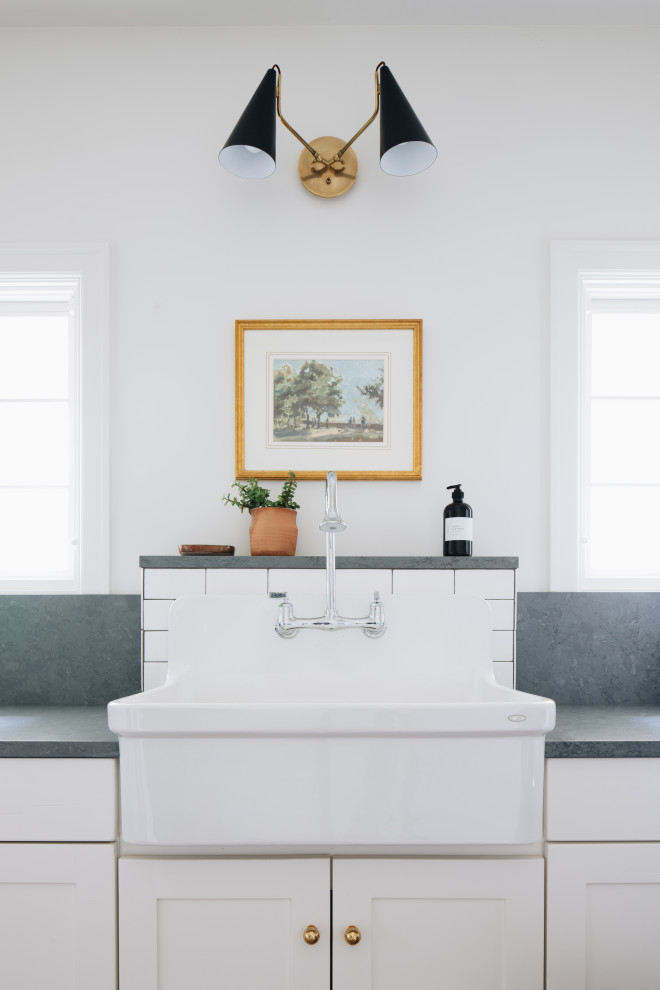 Foto på en vintage gröna l-formad tvättstuga enbart för tvätt, med en rustik diskho, luckor med infälld panel, vita skåp, granitbänkskiva, vita väggar, ljust trägolv, en tvättmaskin och torktumlare bredvid varandra och beiget golv