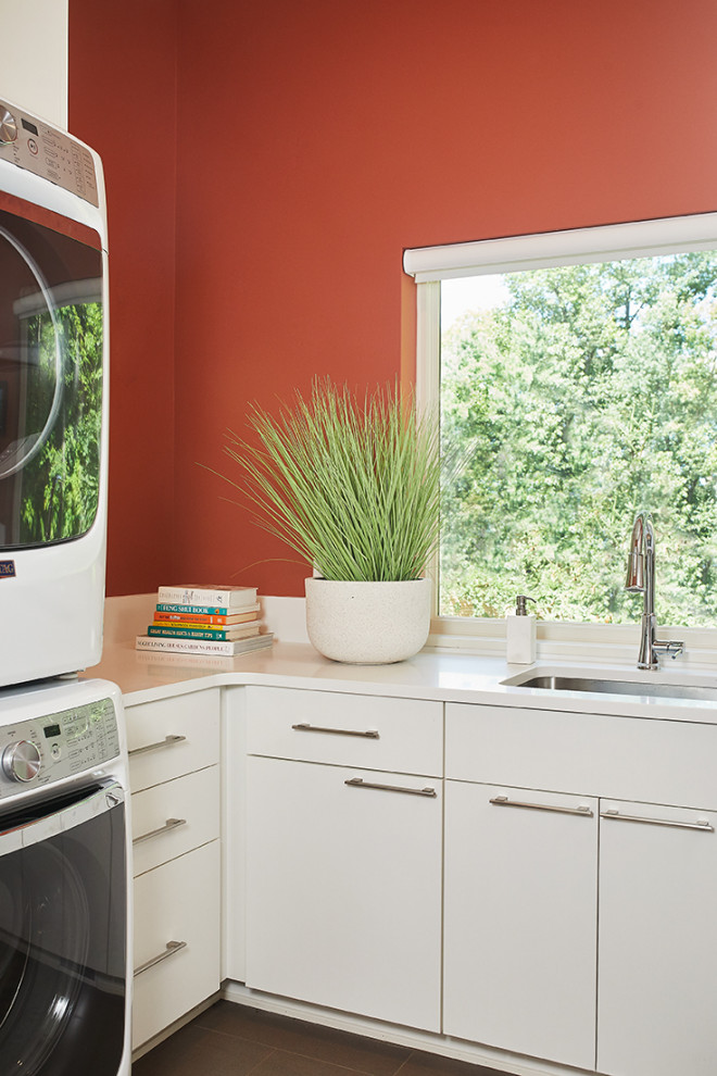 グランドラピッズにある中くらいなミッドセンチュリースタイルのおしゃれな洗濯室 (L型、アンダーカウンターシンク、フラットパネル扉のキャビネット、白いキャビネット、クオーツストーンカウンター、赤い壁、セラミックタイルの床、上下配置の洗濯機・乾燥機、茶色い床、白いキッチンカウンター) の写真