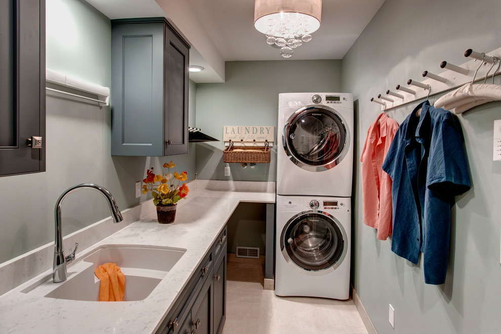 Inredning av en klassisk mellanstor parallell tvättstuga enbart för tvätt, med en undermonterad diskho, skåp i shakerstil, bänkskiva i kvarts, blå väggar, klinkergolv i porslin, en tvättpelare och grå skåp