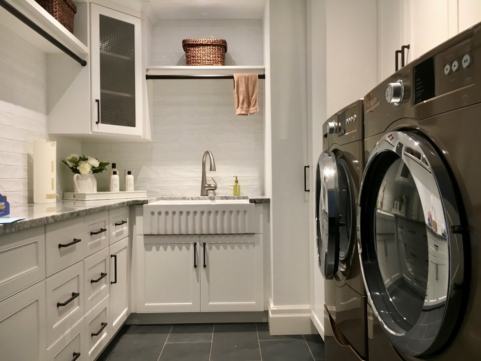 Exempel på en stor klassisk grå u-formad grått tvättstuga enbart för tvätt, med en rustik diskho, skåp i shakerstil, vita skåp, granitbänkskiva, vitt stänkskydd, stänkskydd i keramik, vita väggar, klinkergolv i porslin, en tvättmaskin och torktumlare bredvid varandra och svart golv