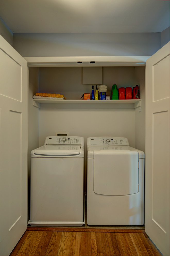 Ejemplo de armario lavadero contemporáneo pequeño con paredes blancas, suelo de madera clara y lavadora y secadora juntas