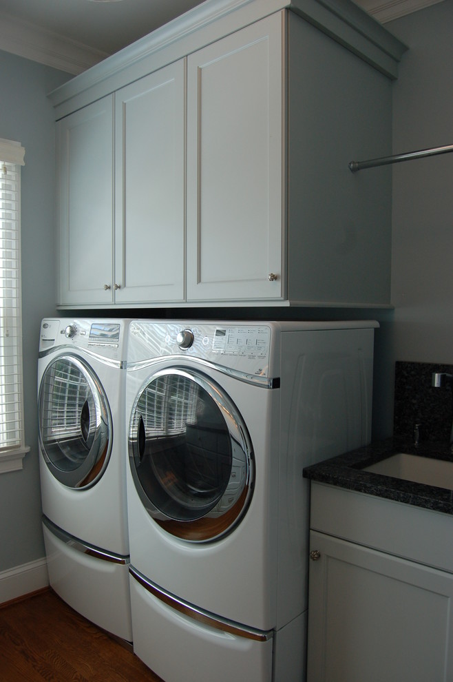 Inspiration för mycket stora klassiska parallella tvättstugor enbart för tvätt, med en undermonterad diskho, luckor med infälld panel, granitbänkskiva, blå väggar, mellanmörkt trägolv, en tvättmaskin och torktumlare bredvid varandra och vita skåp