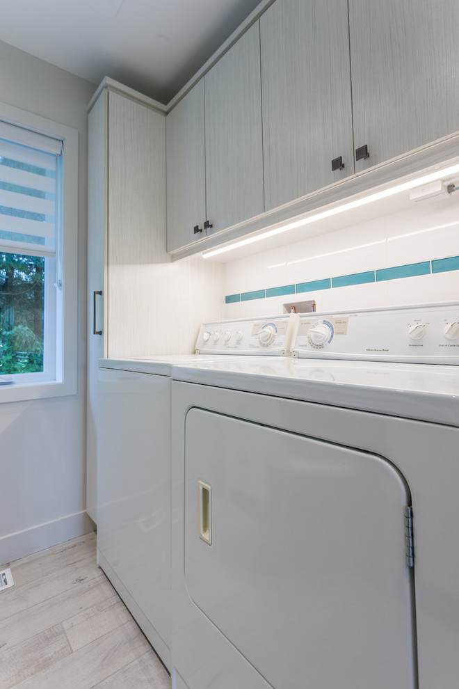 Klassisk inredning av ett litet u-format grovkök, med släta luckor, vita skåp, blå väggar, klinkergolv i keramik, en tvättmaskin och torktumlare bredvid varandra och beiget golv