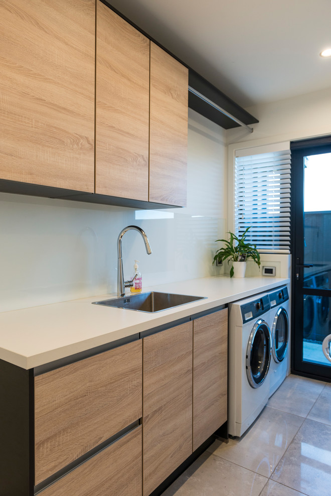 Photo of a medium sized contemporary single-wall separated utility room in Christchurch with a built-in sink, flat-panel cabinets, light wood cabinets, laminate countertops, white walls, ceramic flooring, a side by side washer and dryer and brown floors.
