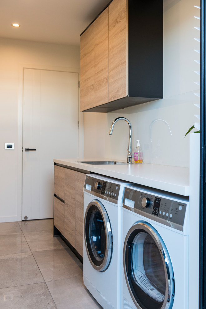Dedicated laundry room - mid-sized contemporary single-wall ceramic tile and brown floor dedicated laundry room idea in Auckland with a drop-in sink, flat-panel cabinets, light wood cabinets, laminate countertops, white walls and a side-by-side washer/dryer