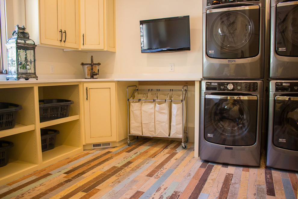 Exempel på en stor amerikansk l-formad tvättstuga enbart för tvätt, med en undermonterad diskho, luckor med upphöjd panel, gula skåp, bänkskiva i kvarts, beige väggar, en tvättpelare och målat trägolv