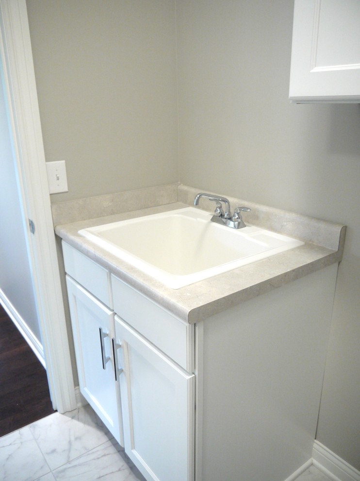 Exempel på en klassisk tvättstuga, med en allbänk, luckor med infälld panel, vita skåp, laminatbänkskiva, grå väggar och klinkergolv i keramik