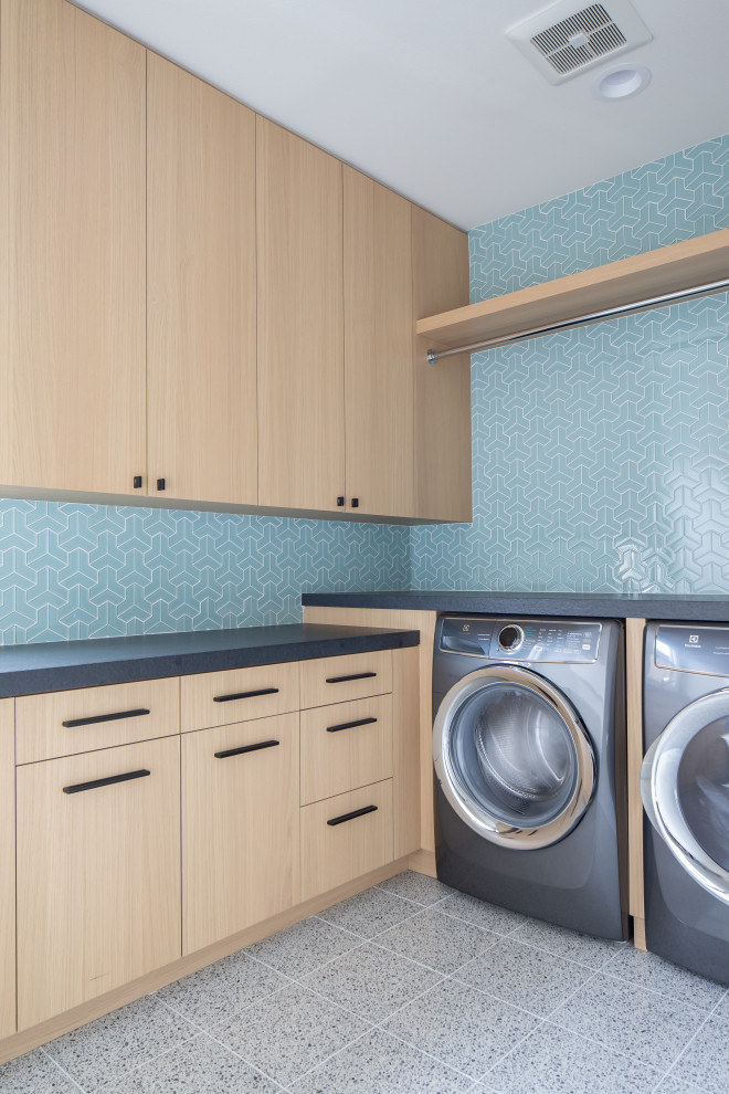 Idéer för funkis l-formade grått tvättstugor enbart för tvätt, med släta luckor, skåp i ljust trä, blå väggar, en tvättmaskin och torktumlare bredvid varandra och grått golv