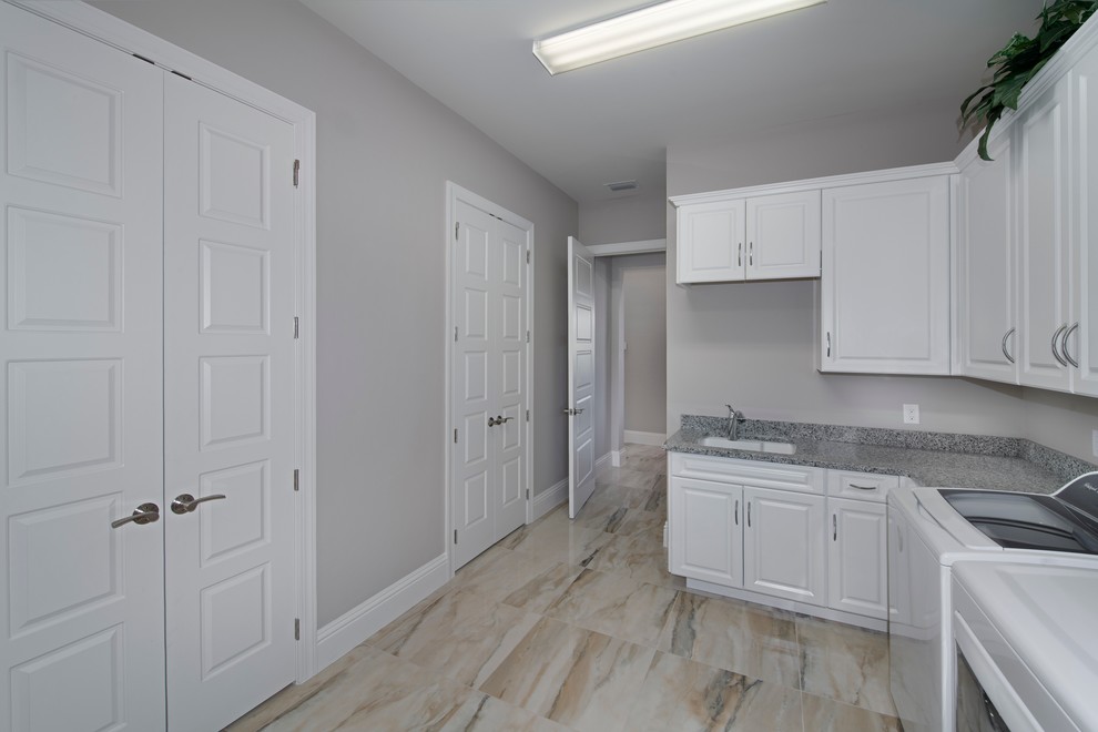 Photo of a medium sized mediterranean l-shaped separated utility room in Miami with a submerged sink, raised-panel cabinets, white cabinets, grey walls, a side by side washer and dryer and beige floors.