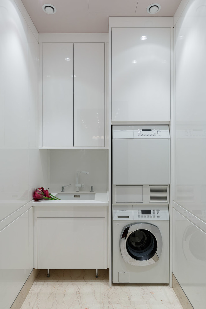 Einzeilige Moderne Waschküche mit Unterbauwaschbecken, flächenbündigen Schrankfronten, weißen Schränken, weißer Wandfarbe und Waschmaschine und Trockner gestapelt in Moskau