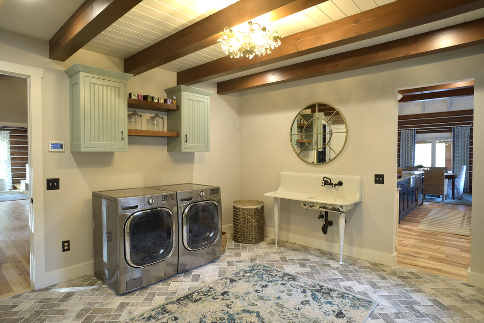 コロンバスにある高級な広いラスティックスタイルのおしゃれな洗濯室 (L型、エプロンフロントシンク、インセット扉のキャビネット、青いキャビネット、グレーの壁、セラミックタイルの床、左右配置の洗濯機・乾燥機、グレーの床) の写真
