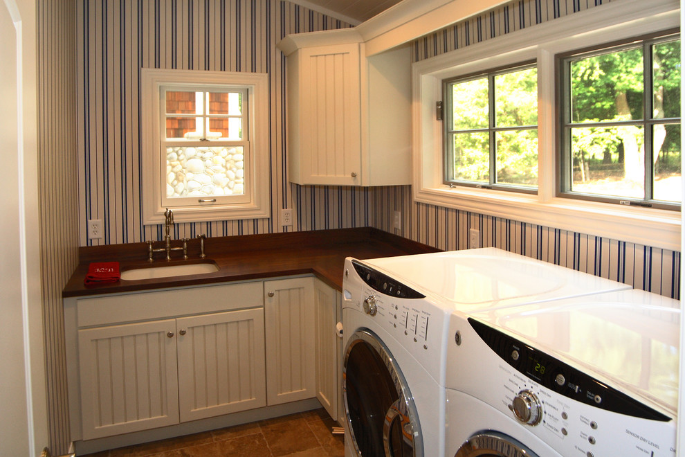 Maritim inredning av en mellanstor l-formad tvättstuga enbart för tvätt, med en undermonterad diskho, skåp i shakerstil, vita skåp, träbänkskiva, klinkergolv i terrakotta, en tvättmaskin och torktumlare bredvid varandra och brunt golv