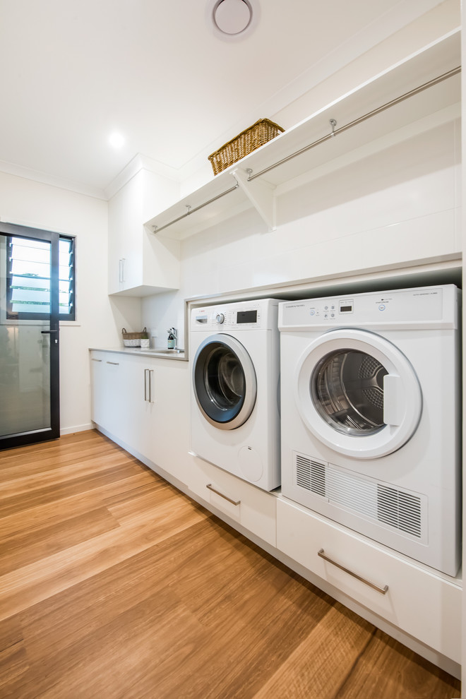 Inspiration for a mid-sized contemporary single-wall vinyl floor dedicated laundry room remodel in Other with a single-bowl sink, flat-panel cabinets, white cabinets, granite countertops, white backsplash, ceramic backsplash, white walls, a side-by-side washer/dryer and gray countertops