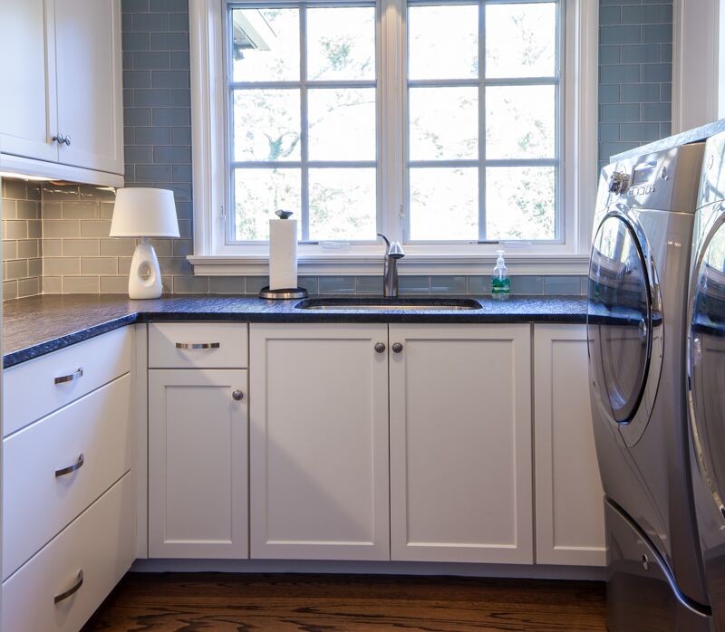 Ejemplo de lavadero multiusos y en L de tamaño medio con puertas de armario blancas, paredes azules, suelo de madera en tonos medios y lavadora y secadora juntas