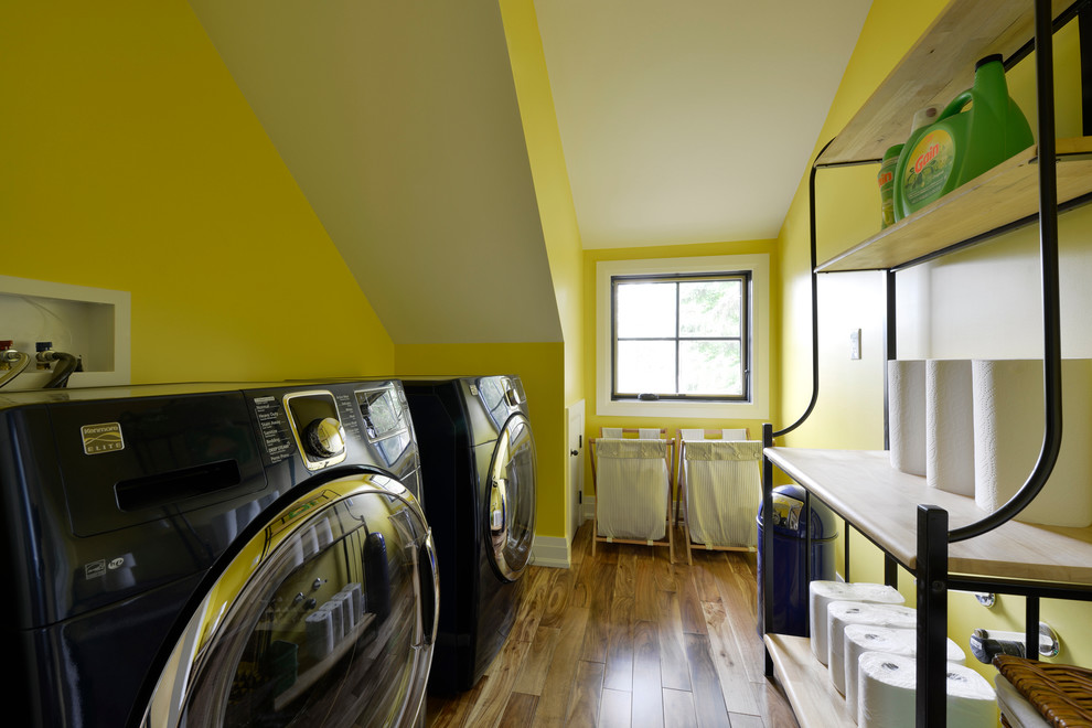 Foto de cuarto de lavado de galera de tamaño medio con paredes amarillas, suelo de madera en tonos medios y lavadora y secadora juntas