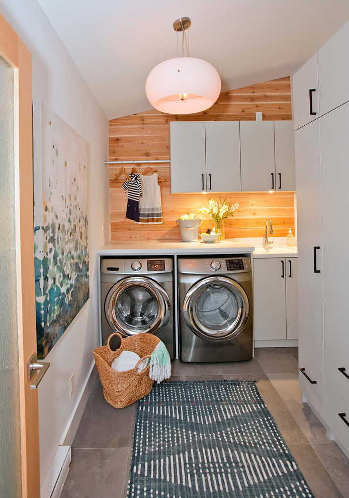 Esempio di una sala lavanderia minimal di medie dimensioni con lavello sottopiano, ante lisce, ante bianche, top in superficie solida, pareti bianche e lavatrice e asciugatrice affiancate