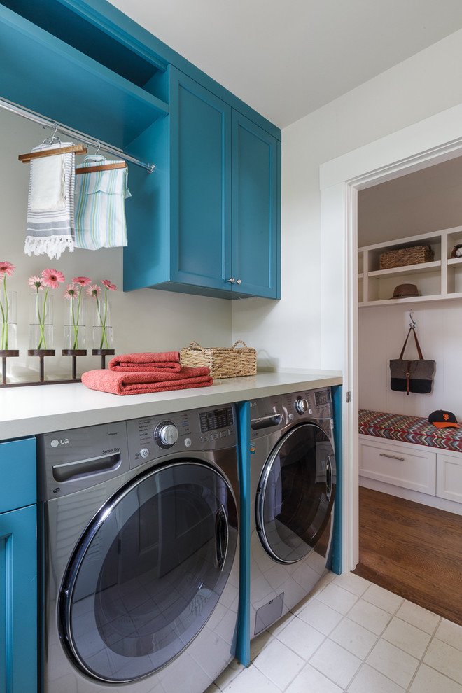 Bild på en liten lantlig linjär tvättstuga enbart för tvätt, med blå skåp, bänkskiva i kvarts, klinkergolv i porslin, en tvättmaskin och torktumlare bredvid varandra, luckor med infälld panel och grå väggar