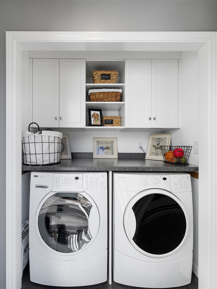 Cette image montre une buanderie linéaire traditionnelle de taille moyenne avec un placard, un placard à porte shaker, des portes de placard blanches, un plan de travail en stratifié, un mur blanc et des machines côte à côte.