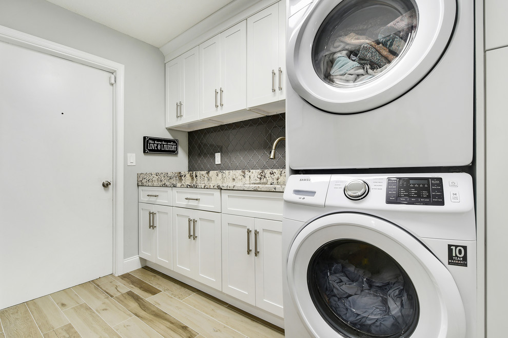 Mid-sized trendy galley ceramic tile and gray floor dedicated laundry room photo in Miami with an undermount sink, shaker cabinets, white cabinets, granite countertops, gray walls, a stacked washer/dryer and multicolored countertops
