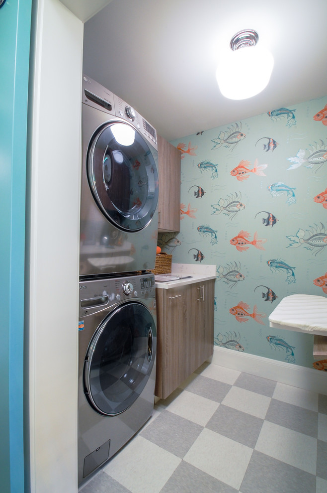 ミネアポリスにあるラグジュアリーな中くらいなビーチスタイルのおしゃれな洗濯室 (ll型、アンダーカウンターシンク、フラットパネル扉のキャビネット、大理石カウンター、青い壁、リノリウムの床、上下配置の洗濯機・乾燥機、中間色木目調キャビネット) の写真