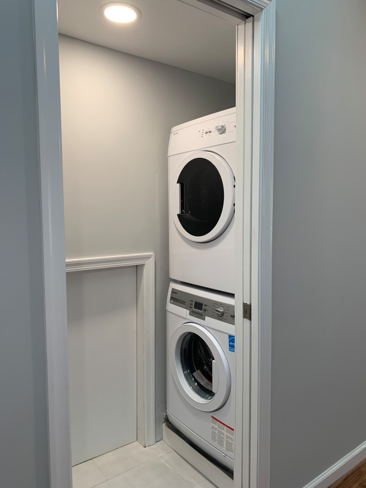 Example of a small trendy single-wall ceramic tile and white floor laundry closet design in DC Metro with white walls and a stacked washer/dryer