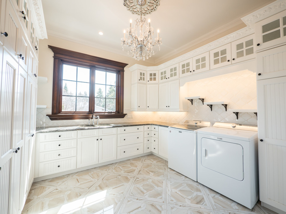Inredning av en klassisk stor vita u-formad vitt tvättstuga, med en undermonterad diskho, luckor med infälld panel, vita skåp, marmorbänkskiva, klinkergolv i porslin och vitt golv