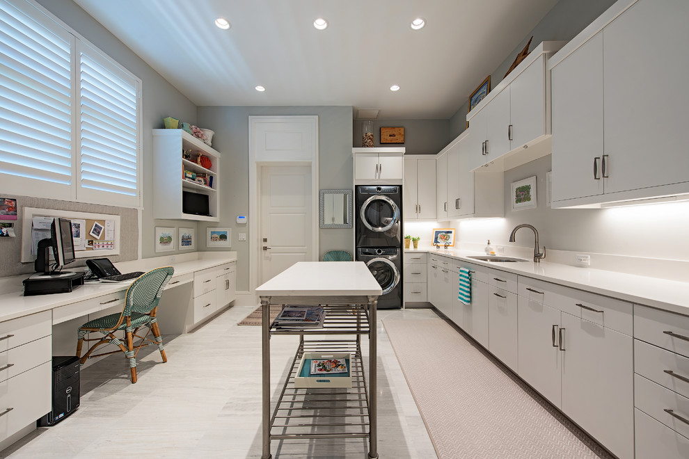 Contemporary u-shaped utility room in Miami with white worktops, a submerged sink, flat-panel cabinets, white cabinets, grey walls, a stacked washer and dryer and grey floors.