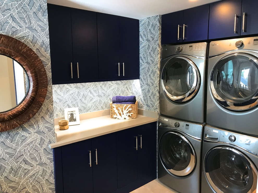 Photo of a large beach style l-shaped separated utility room in Philadelphia with a submerged sink, flat-panel cabinets, blue cabinets, engineered stone countertops, blue walls, porcelain flooring and a stacked washer and dryer.